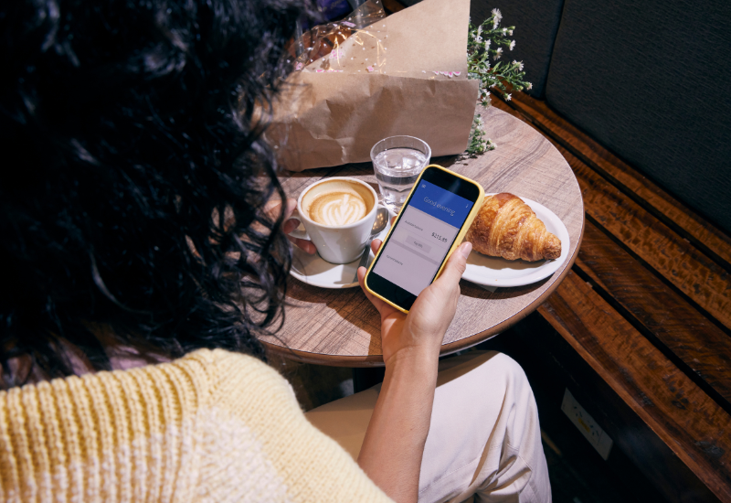 Budget Insights Woman sitting at a café checking her budget on a smartphone while enjoying coffee and a croissant.