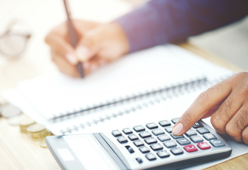 NDIS Budget Planning with Calculator and Notes Person calculating a budget using a calculator and notebook with coins nearby on a desk.