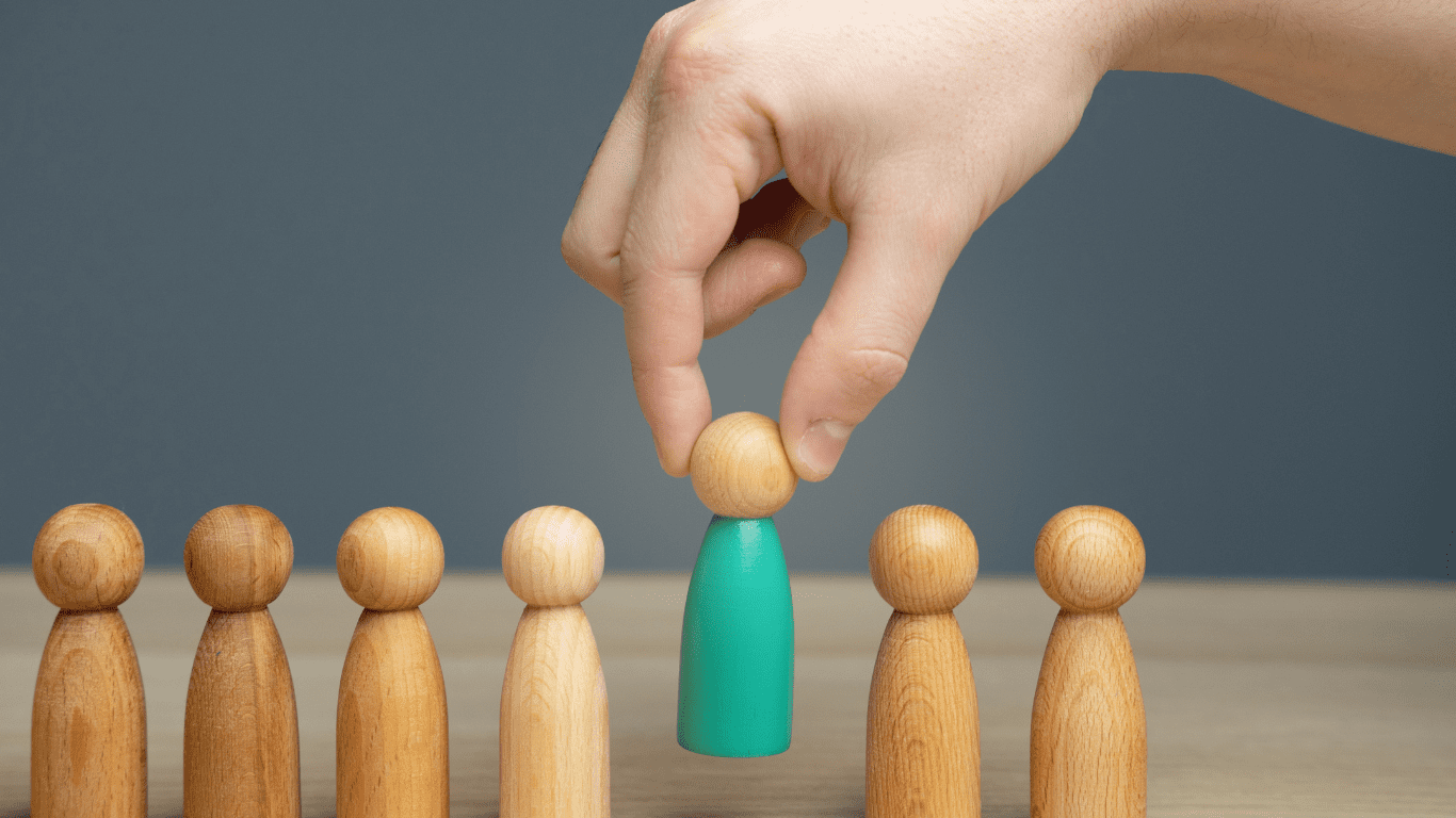 A hand selecting a green wooden figure from a row of wooden pegs, symbolizing choosing the right NDIS support worker.