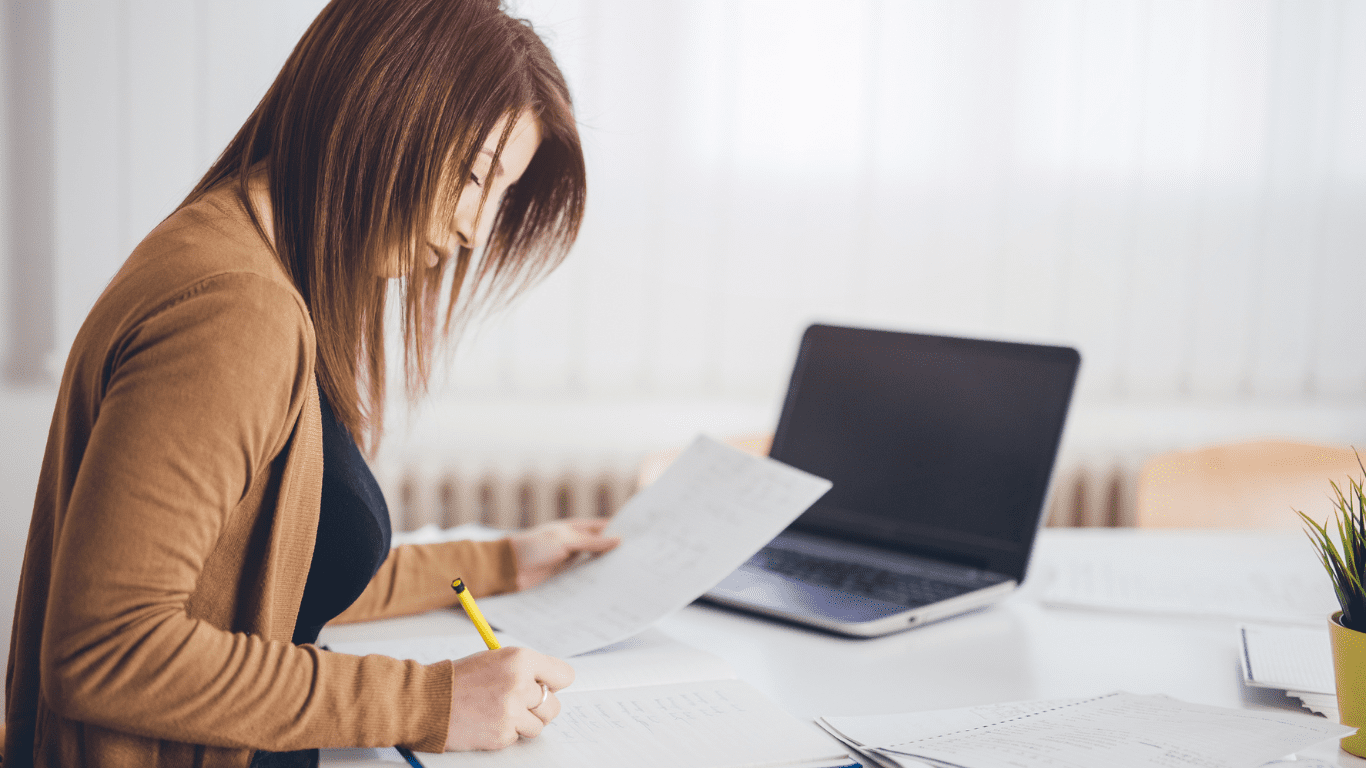 A participant reviewing and organising NDIS paperwork at a desk with a laptop.