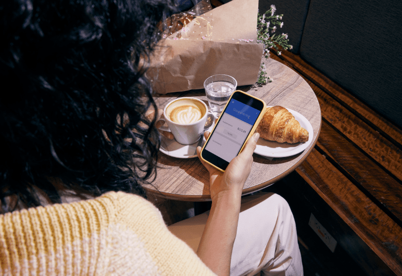 Budget Insights Woman sitting at a café checking her budget on a smartphone while enjoying coffee and a croissant.