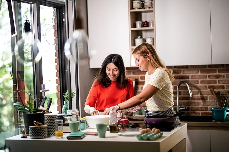 Cooking Activity with NDIS Support Worker Two women smiling and preparing food together in a bright, modern kitchen.